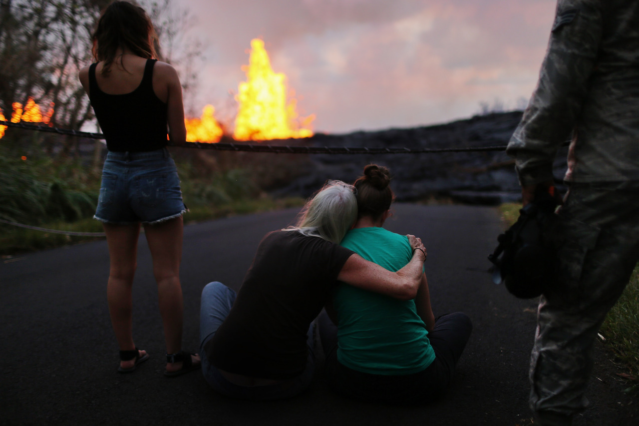 [写真]キラウエア火山の噴火で、住宅を飲み込みながら流れ進むマグマを前に座り込む人々（Photo by GettyImages）